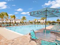 The pool area at our townhomes in Apopka, FL, featuring reclining chairs, palm trees, and a view of the townhomes.