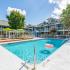 Community pool with wooden deck, grey lounge chairs, white fence, surrounded by the community buildings.