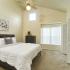 Beige carpeted bedroom with white comforter place on bed.  Folding closet door is open, exposing storage area.