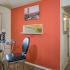 Dining area with high top dining table and chairs, orange accent wall, and hallway leading to other areas of the apartment.