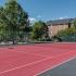 Red colored tennis court with trees and building in background.