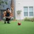 Young man playing boccie ball with building in background.