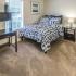 Carpeted bedroom with made bed, dark stained wood desk, tall dresser, nightstand with lamp.