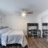 Bedroom with wood style flooring bed, desk with chair, nightstand with lamp, and ceiling fan.