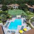 Overhead photo of community pool lined with lounge chairs, palm trees.  Tennis court, basketball court, and apartment buildings in the background.