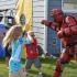 Several children holding padded clubs are smiling and attacking a man wearing red plastic armor. A blue dunk tank sits in the background. | Delta Junctions Rentals | Fort Greely rentals| DOD housing
