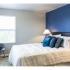 Bedroom split with dark blue and light grey paint. Large bed in the middle and a corner chair across from the bed. Light grey carpet