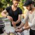 two men cooking fish and vegetables on a grill outdoor.