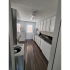 Kitchen with wood flooring and white cabinets featuring a sink, stove, and dishwasher on a long wall. A fridge and door to the outside of the home is on an adjacent wall to the stove. Washer and dryer in kitchen.