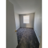 Carpeted room with gray walls and a square window on the wall opposite of the door bringing in natural light.