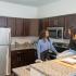 Block75 Apartments, interior, kitchen, two women talking and smiling, brown cabinets, breakfast bar counter, stainless steel appliances, refrigerator, microwave, stove/oven