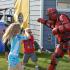 Several children holding padded clubs are smiling and attacking a man wearing red plastic armor. A blue dunk tank sits in the background. | Delta Junctions Rentals | Fort Greely rentals| DOD housing