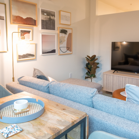 Small dining area within living space that features grey sofa and large HDTV on entertainment center in a Modera Broadway apartment.