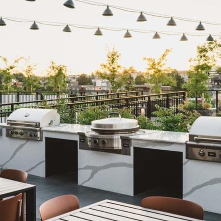 3 grilling stations and outdoor dining area under lights on a rooftop filled with greenery at Modera Broadway apartments.