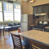 Crescendo Apartments, interior, kitchen, dining room, living romo, breakfast bar counter, stainless steel appliances, dark cabinets, large windows, dining set, leather couch, stylishly exposed industrial venting