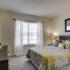 Furnished bedroom with wall-to-wall carpeting and oversized window with mini-blinds. Room includes king-sized bed, nightstand, horizontal dresser with large mirror above. at Summit Place apartments in Methuen, MA.