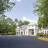 Paved entry with parking lot and clubhouse surrounded by trees and landscaping