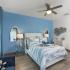 Bedroom with wood style flooring and blue accent wall.  Bed has a blue and white comforter and breakfast tray on it.  Ceiling fan and entrance into bathroom are also present.