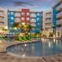 Dusk photo of community pool surrounded by multi-colored pavers, colorful lounge chairs, palm trees, and four floors of balconies on each side.