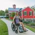 Swallowtail Flats at Old Town Exterior: Red Building with multiple windows, Long path with landscaping, Girl with flower dress in a wheelchair on the path