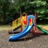 Outdoor Playground Structure: slide, climbers, playhouse, picnic table.