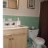 Bathroom with white tile floors, green tile on the wall, a sink and a toilet