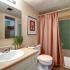 Lenox Apartments Inc, interior, bathroom, white, cream, green tile, peach shower curtain, large mirror, shower/tub, toilet, sink,