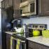 Dark cabinets. granite counter top, with silver appliances. A bright green basket and kettle pot