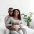 african american couple wife is pregnant they are sitting on bedroom