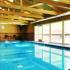 Indoor heated swimming pool with vaulted wood beamed ceiling and one wall made of glass.