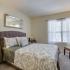 Furnished bedroom with plush carpeting and oversized window with mini-blinds. Room includes queen-sized bed, two nightstands, chair, lamp and horizontal dresser. at Summit Place apartments in Methuen, MA.