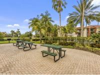 Three outdoor picnic benches with barbecue grill near pool area surrounded in palm trees
