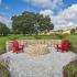 The Lodge at Woodlake apartments, exterior, stone fire pit, apartment exteriors, red lounge chairs, large grassy area and trees