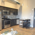 Crescendo Apartments, interior, kitchen, wood floor, dark cabinets, stainless steel appliances, refrigerator, oven/stove, microwave, dishwasher, table and chairs, gray front door, industrial vent pipe towards ceiling